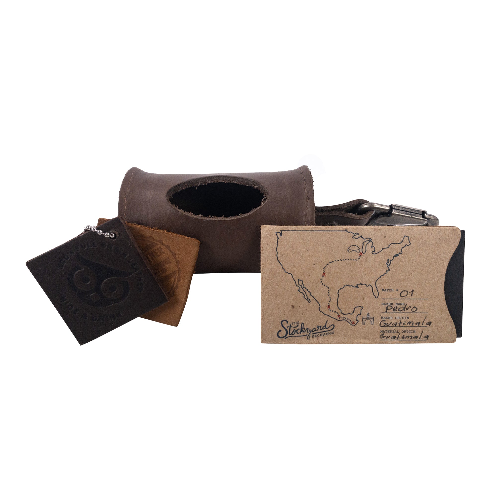 Showcasing the Doggie Bag Dispenser by Hide & Drink along with its tags, highlighting the product's made from thick full grain leather and small batch production. This stylish poop bag holder is perfect for dog walkers and is handmade in La Antigua Guatemala.