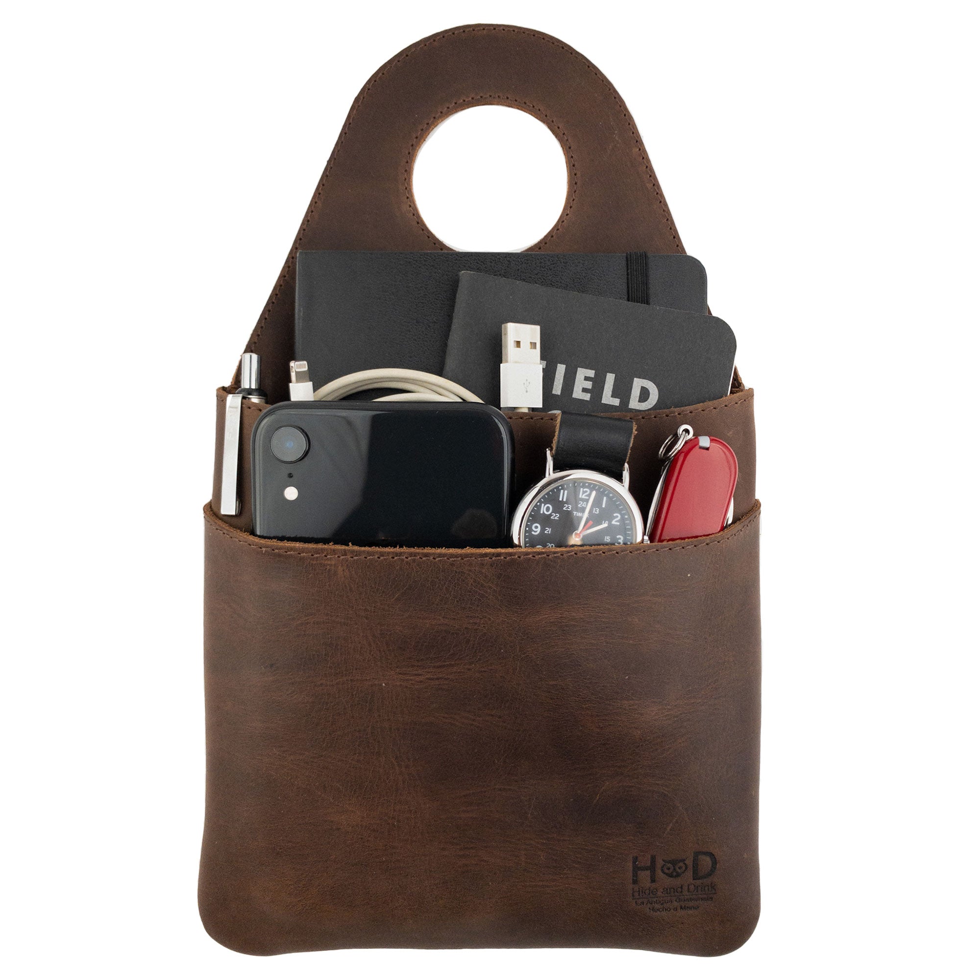 Hide & Drink's Seat Side Organizer for Gear Stick filled with essentials like chargers and small items, made from premium Full Grain Leather. This holder is not only practical for organizing but also an outdoor protector for knives. It's a handmade product created through small batch production, emphasizing hand cut, hand sewn quality by artisans in La Antigua Guatemala & Oaxaca Mexico.
