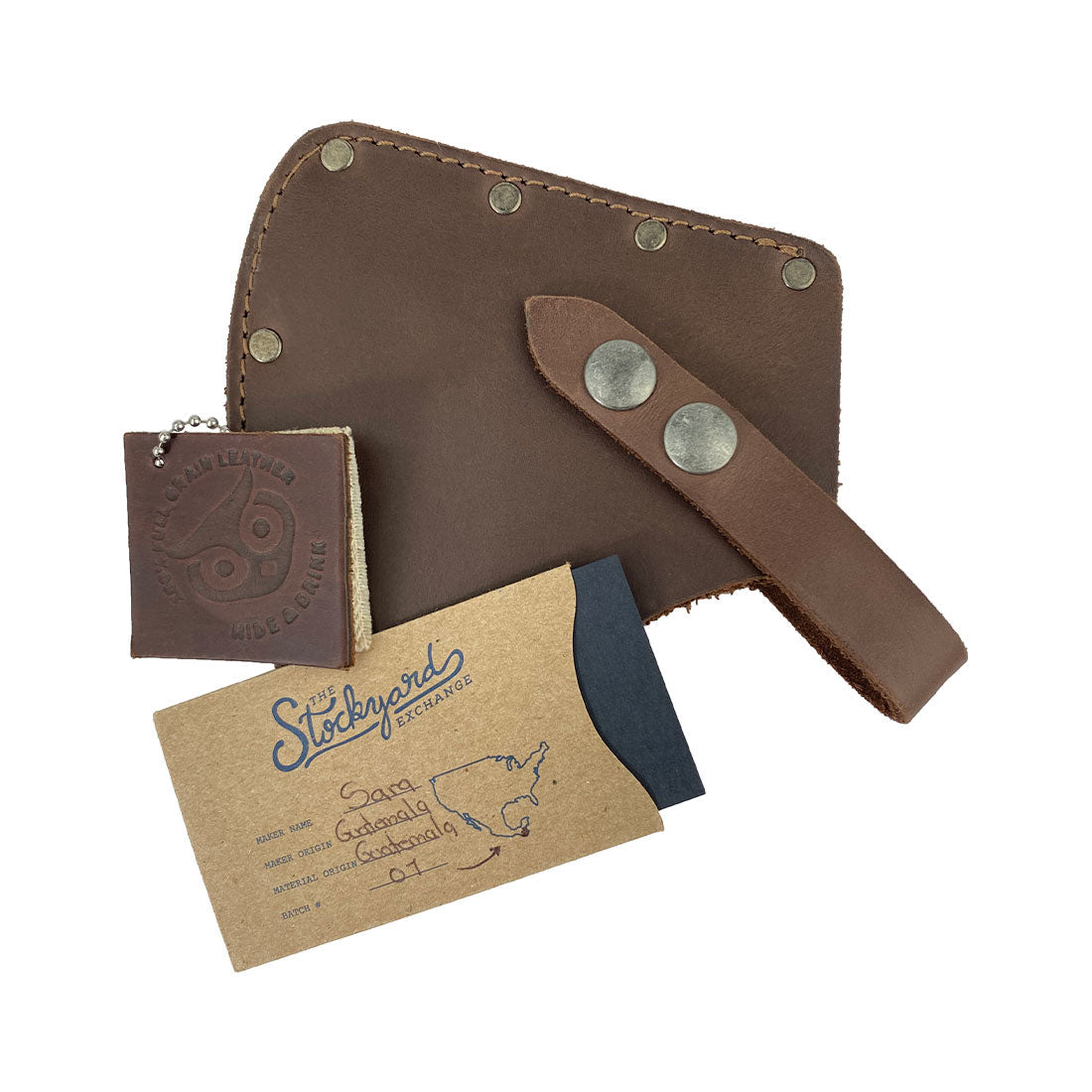Camper Axe Head Sheath by Hide & Drink displayed along with a business card and wallet, highlighting its design as an Adjustable Axe Sheath. This Full Grain Leather protector case cover functions as a blade sleeve for camping accessories, representing artisan craftsmanship, small batch production, and handmade quality from La Antigua Guatemala & Oaxaca Mexico.