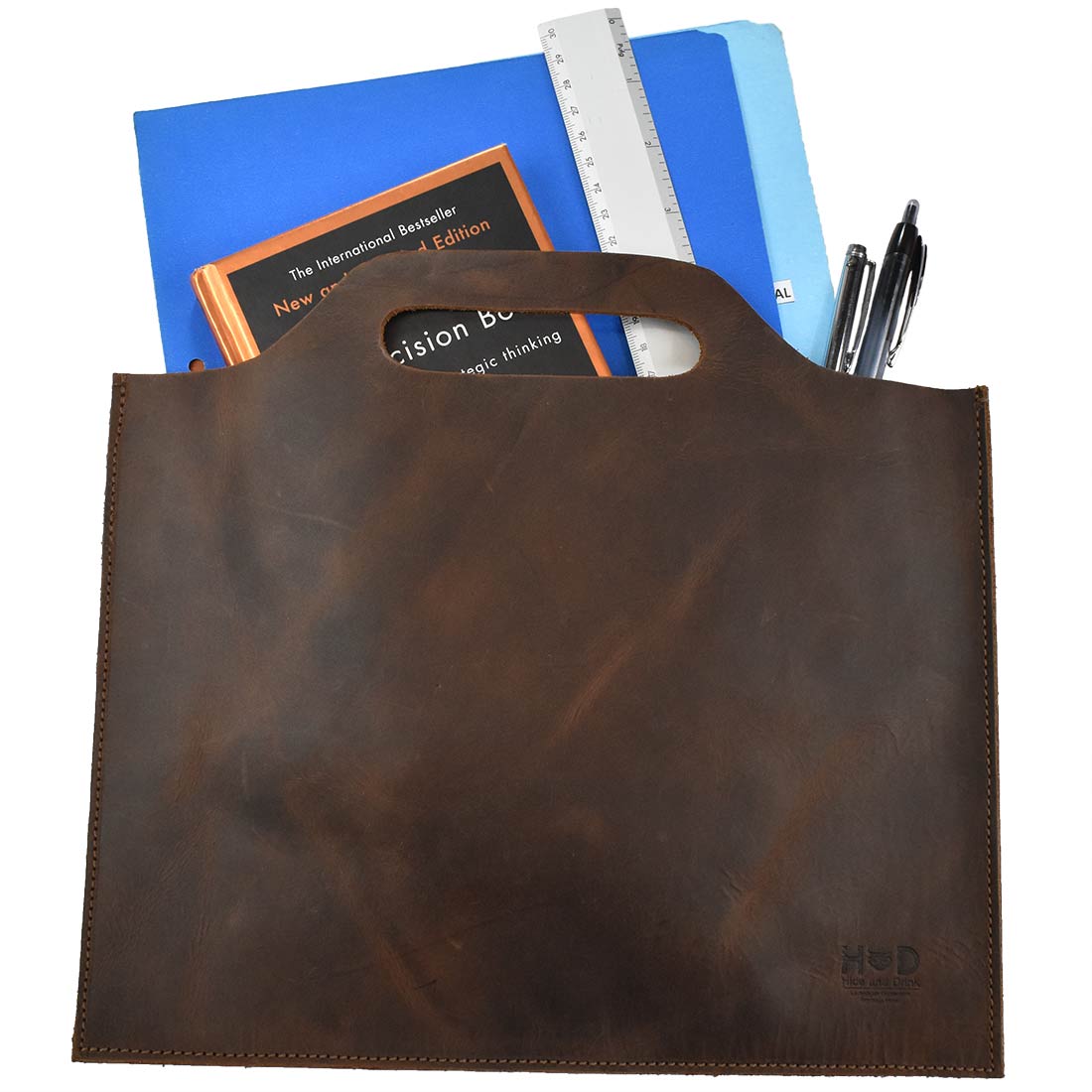Flat Handbag by Hide & Drink displayed with documents and pens, emphasizing its functionality as a thin portfolio and classic document holder. Made from full grain leather, this minimalist style carry-on bag is a stylish travel accessory. Each bag is meticulously hand cut, hand sewn, and fire branded, showcasing artisan craftsmanship from La Antigua Guatemala & Oaxaca Mexico.