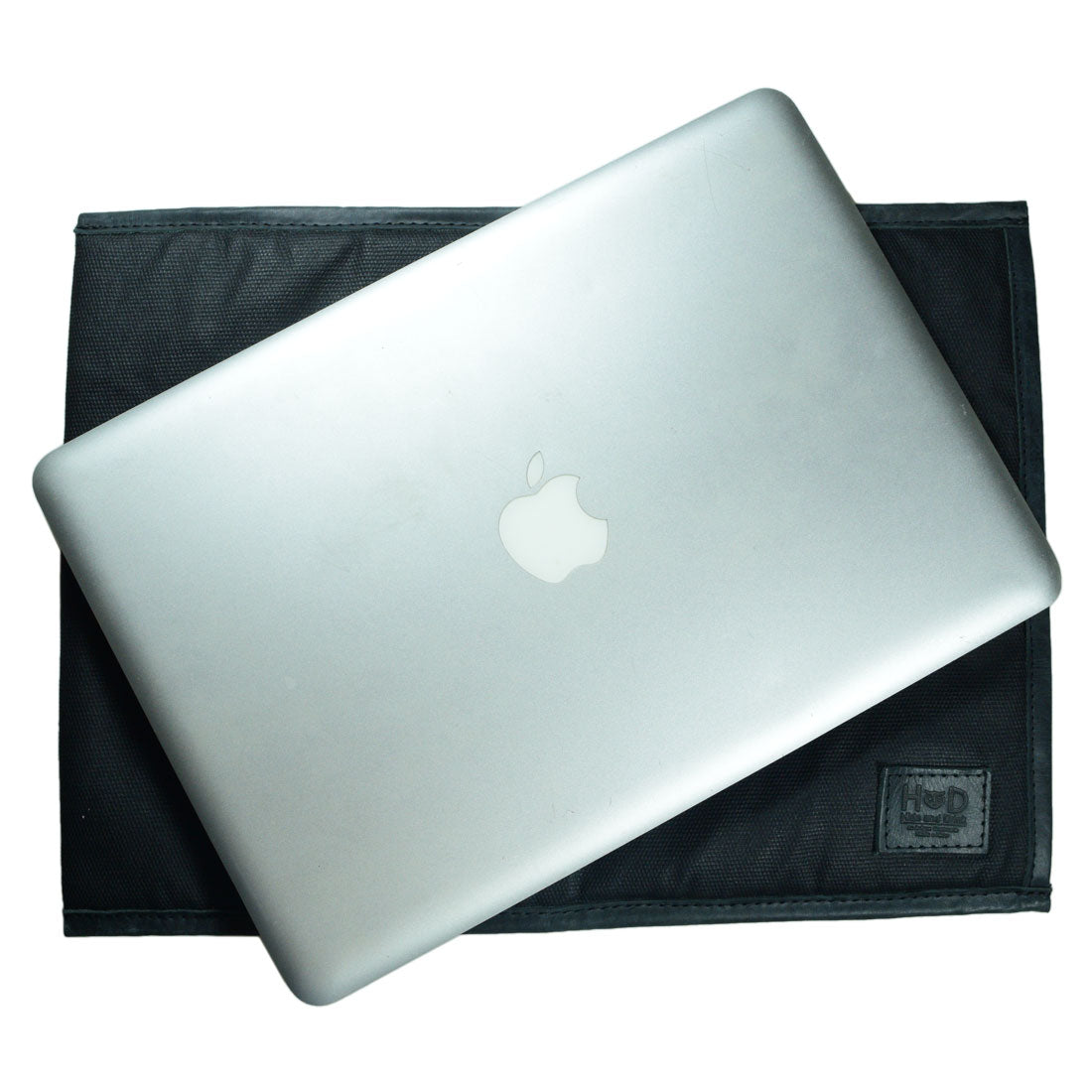 Overhead view of Laptop Sleeve 14 in. by Hide & Drink with a MacBook on top. This stylish and rugged sleeve is compatible with MacBook Air/Pro 13 Inch with M1 Chip, handcrafted from Waxed Canvas, ensuring durability through small batch production, hand cut, hand sewn, and fire branded techniques by artisans in La Antigua Guatemala & Oaxaca Mexico.