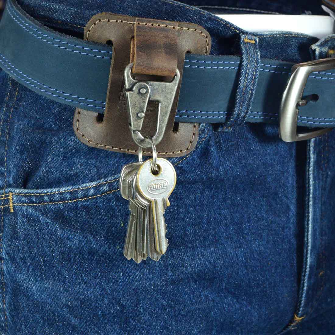 A close-up image of a Belt Key Holder from Hide & Drink, showcasing a classic vintage keychain organizer attached to a blue belt, ideal for keeping keys secure. This accessory is made from durable full grain leather, representing small batch production, hand cut and sewn by artisans in La Antigua Guatemala & Oaxaca Mexico.